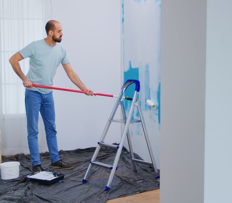 a boy is painting interior wall with roller