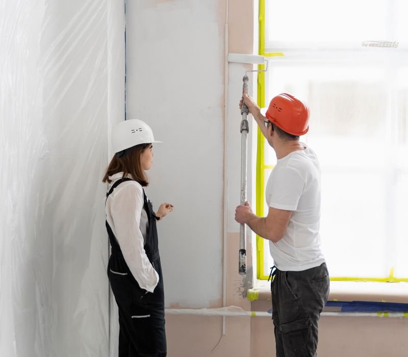 a boy is painting wall and girl is watching him standing besides him