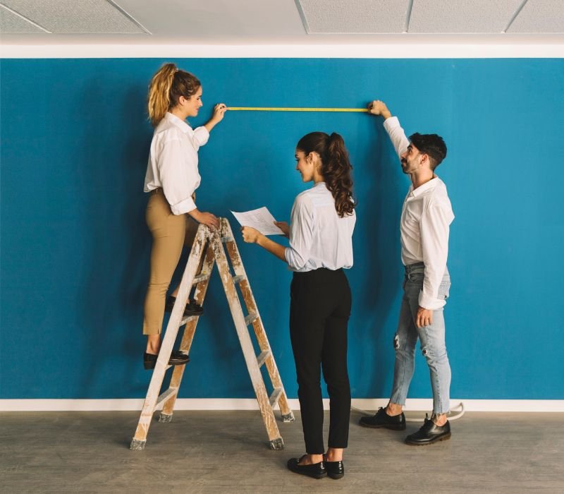 group of two girls and one boy measuring wall for paint