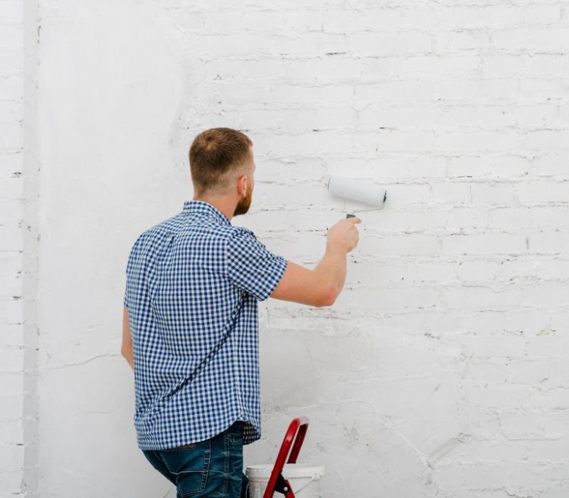 a boy painting wall with roller standing on ladder