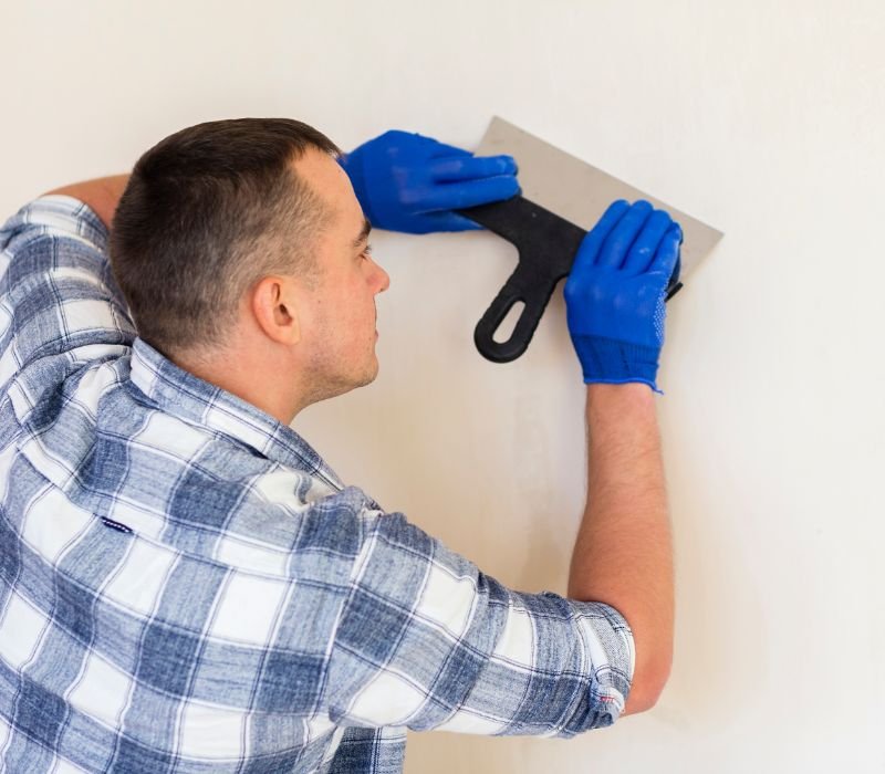 a boy is removing wallpaper with scraper